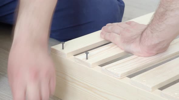 Assembling furniture, the carpenter screws the screw into the boards with a screwdriver