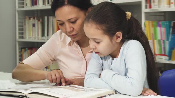 Asian Mature Woman Reading a Book with Her Cute Litlle Daughter 