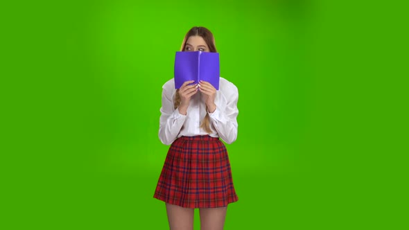 Schoolgirl Covered Her Face with a Violet Notebook. Green Screen