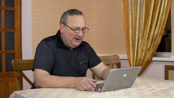 A Man Communicates with Friends Via Video Calling Through a Laptop. An Old Man Communicates While