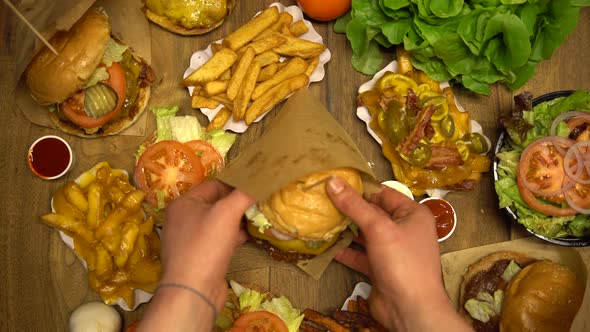 Serving Burger in a Paper Wrap on a Table Full of Fast Food Dishes