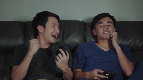 two man playing video games while sitting on sofa. win and lose emotions