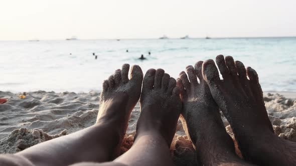 POV Feet of a Couple of Men and Women Lying on a Sandy Beach at Sunset By Ocean