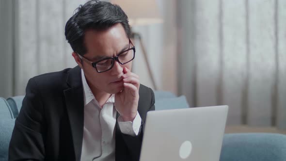 Close Up Of Asian Businessman In Jacket And Shorts Being Tired While Working With A Laptop At Home