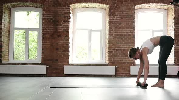 Young Slim Caucasian Woman in Sportswear Rolling Up Yoga Mat on Floor at Gym