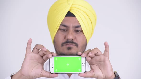 Face of Happy Indian Sikh Businessman Thinking While Showing Phone