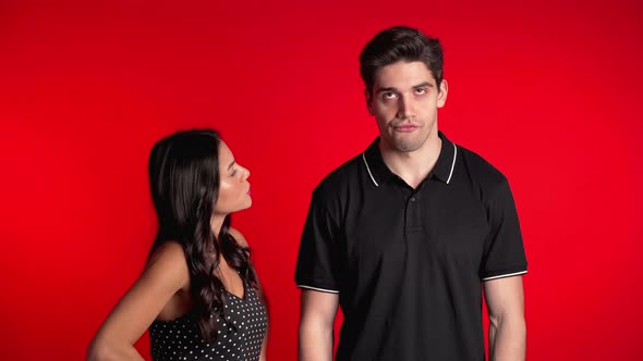 Young Woman Emotionally Scolds Her Boyfriend on Red Background in Studio. 