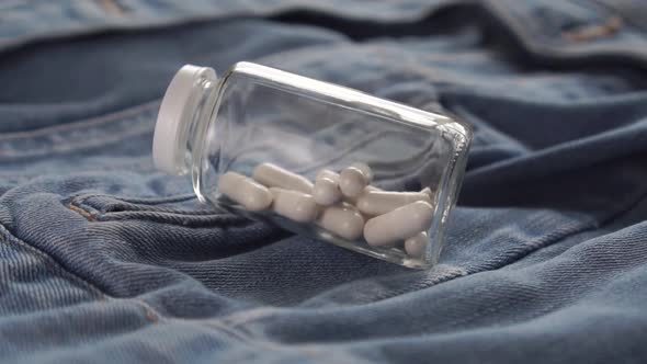 bottle with white medical capsules drops on blue jeans. 