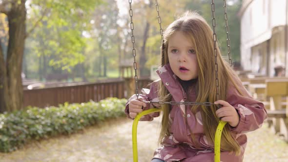 Cute Little Caucasian Girl Talks Then Looks Around As She Sits on a Swing Ride