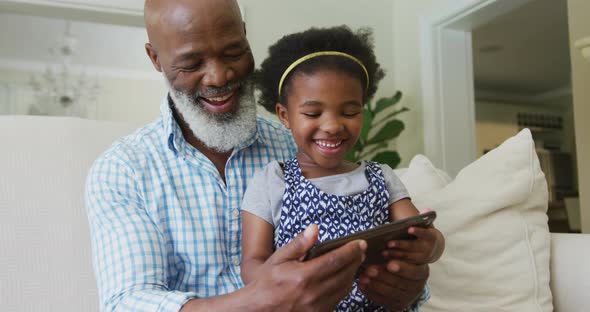 Happy african american grandfather with granddaughter using tablet in living room