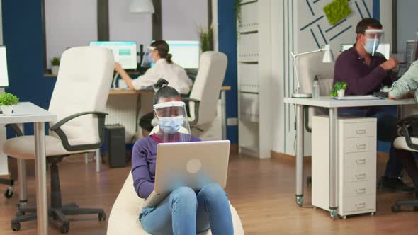 African Employee with Visor Sitting on Armchair in Middle of Office