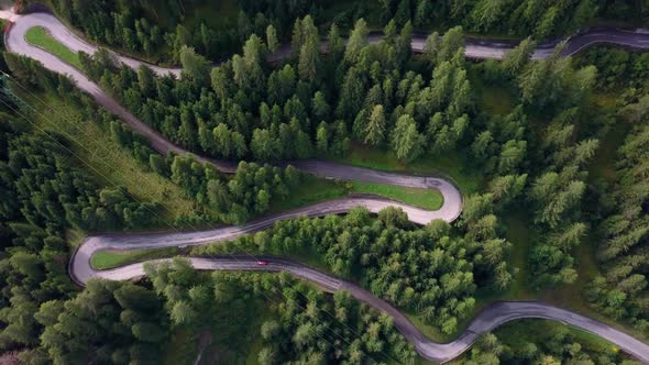 Winding road in the Dolomite mountain park northern Italy with red car advancing, Aerial drone bird'