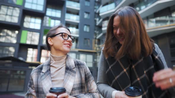 Two Happy Women Walking with Takeaway Coffee and Talking with Interest Among Themselves in the