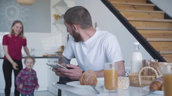 Cheerful Young Woman and Little Girl Running To Busy Man Using Tablet and Hugging Adorable Father