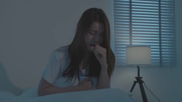 Asian beautiful girl in pajamas feeling bad with fever and coughing after wake up on bed at night.