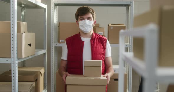 Man Wearing Red Vest Holding Parcels Employee of Warehouse in Medical Face Mask Holds Delivery Boxes