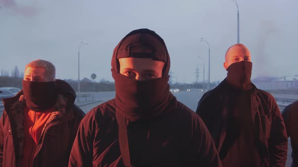 Group of Young Men in Balaclavas with Red Burning Signal Flare on the Road