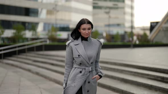 Confident Brunette Lady in Grey Coat is Walking in Downtown in Business Center of City