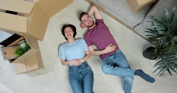 Happy but Tired Young Couple Lie on the Floor of Their New Home