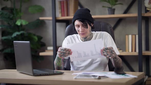 Troubled Male Tattooed Analyst Tearing Paperwork Thinking Sitting in Home Office on Covid19 Pandemic