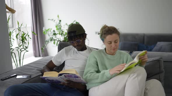 Young Mixed Couple Sitting on Their Couch and Reading Books