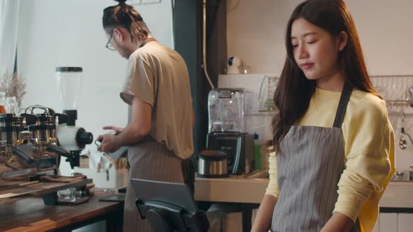 Young Asia female barista taking order by mobile phone and digital tablet standing behind