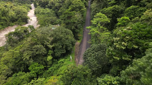 Ascending dronie shot of young man sitting on a motorcycle on the side of a jungle road in Costa Ric