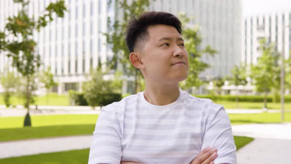 A Young Asian Man Looks Around in an Urban Area  a Park and Office Buildings