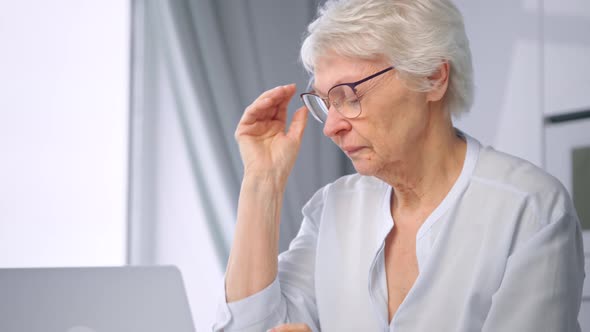 Exhausted overworked old businesswoman with short grey hair takes glasses off