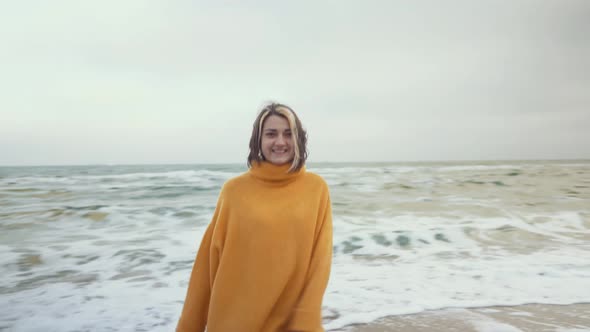 Young Beautiful Woman in Orange Sweater Walking on the Beach in Cold Weather