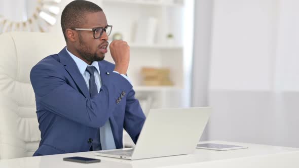 Sick African Businessman with Laptop Coughing in Office