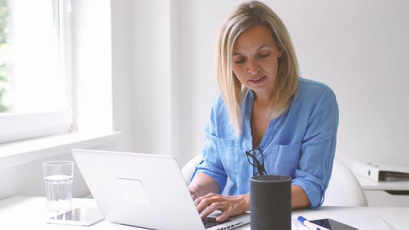 Businesswoman using smart speaker and laptop at home
