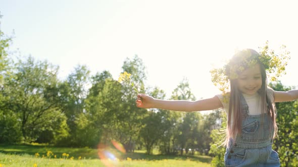 Cute Little Girl in a Flower Wreath on Her Head Jumps and Rejoices Among Dandelions in a Spring