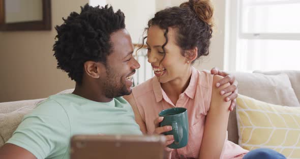 Happy biracial couple sitting on sofa and having video call on smartphone