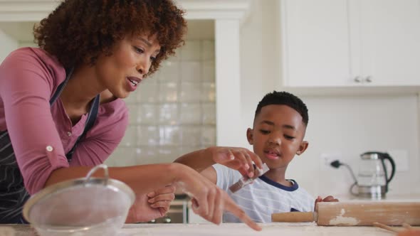 African american mother and son in kitchen cooking, cutting dough