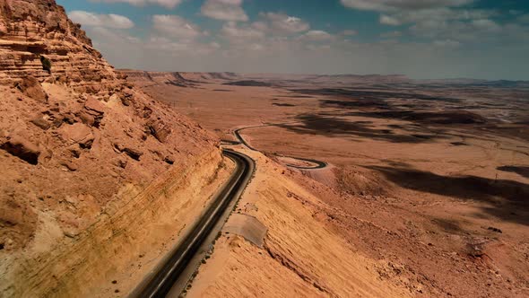 Car Driving on Asphalt Road Through the Desert Sands of the Blue Sky White Clouds