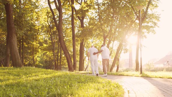 African-American caregiver is teaching disabled old man to walk with walker. Nurse and patient.