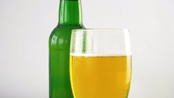 Close up of bottle of beer and glass rotating on white background. 4k footage.