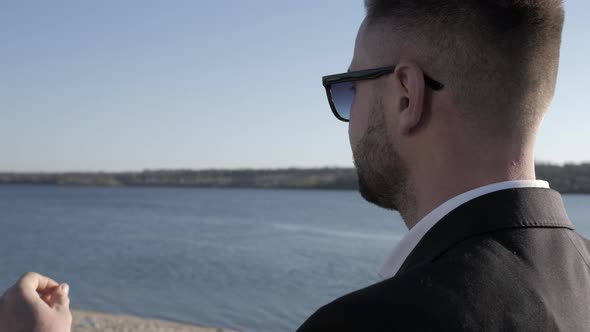 Businessman Takes Off Glasses By the River, View From the Back.