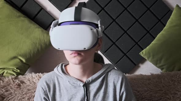 Young Woman Sitting on Sofa Playing Game Using VR Helmet Indoor at Home