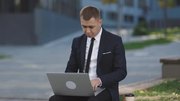 Businessman in Suit and Tie Communication While Typing on Laptop Sitting Outside