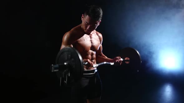 Asian Weightlifter Training Biceps with a Barbell, Black Smoke Background, Slow Motion