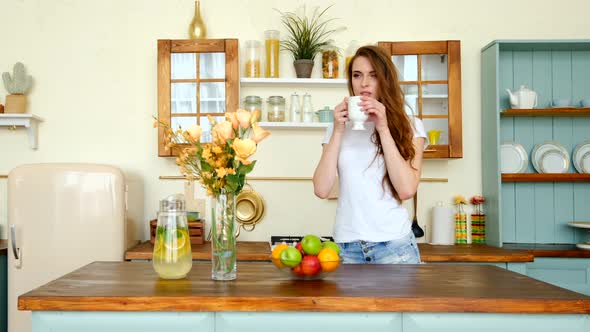 Pensive Young Woman With Long Curly Hair Sipping Coffee In The Kitchen