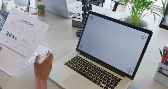 Hands of businesswoman reading report and using laptop at desk in office, copy space on screen