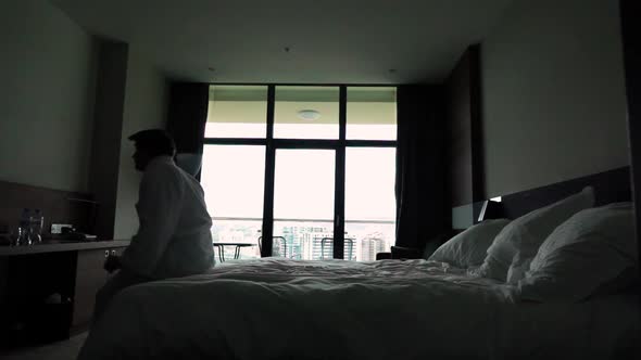 Happy Young Man Jump on Bed at Hotel in Bathrobe