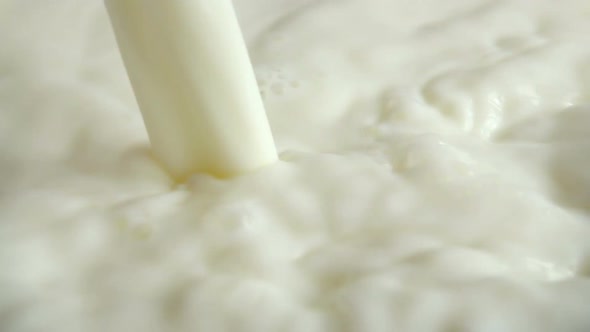 A pouring stream of milk into the milky surface. Slow motion.