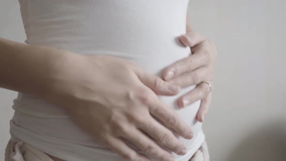 Pregnant Woman in White T-shirt Is Stroking Her Belly. Cozy Home Background.