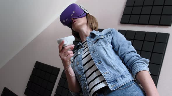 Young Woman in a VR Helmet Plays a Game at Home