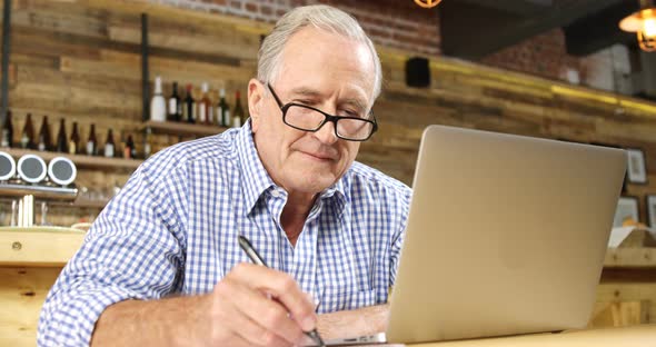 Senior man writing down while using laptop 
