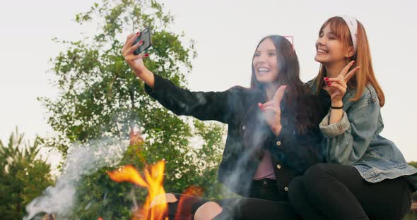 Attractive Multiracial Two Young Girls Around Burning Camping Bonfire In The Woods Taking a Selfie